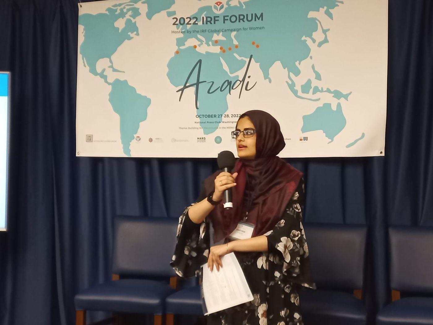 Maryam speaking in front of a world map